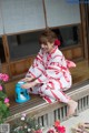 A woman in a red and white kimono sitting on a porch.