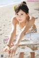 A woman in a bikini sitting on a bench on the beach.