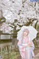 A woman in a kimono holding an umbrella in front of a tree.