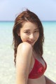 A woman in a red bikini sitting on the beach.