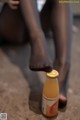 A woman sitting on the ground next to a bottle of orange juice.