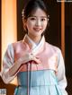 A woman in a pink and blue hanbok poses for a picture.