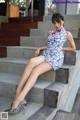 A woman in a blue and white dress sitting on some steps.