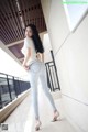 A woman in a white shirt and jeans leaning against a wall.