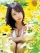 A woman in a white bikini sitting in a field of sunflowers.