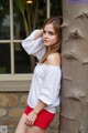 A woman leaning against a tree wearing red shorts and a white shirt.