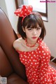 A woman in a red and white polka dot dress sitting on a brown chair.