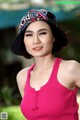 A woman in a pink tank top and a black hat.