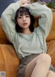 A woman sitting on a couch wearing a green sweater.