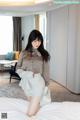 A woman in a gray shirt and skirt posing on a bed.